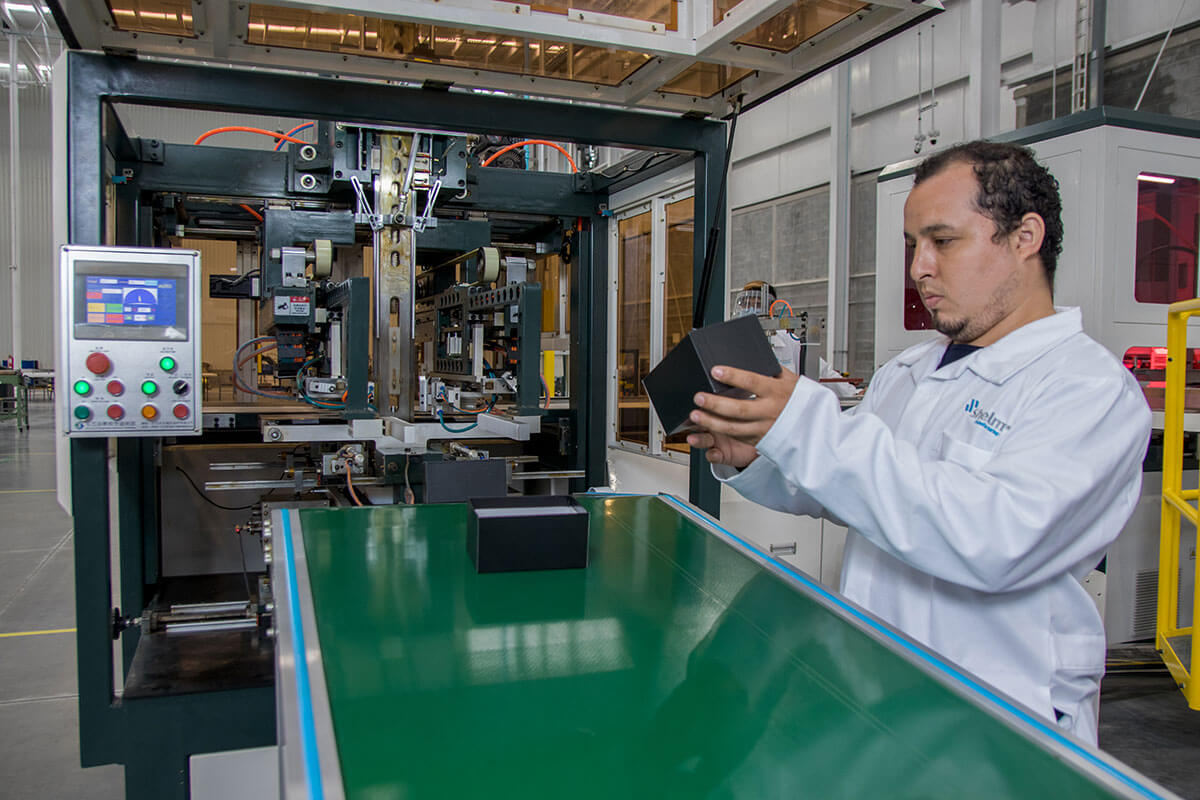 Technician operating production equipment beside a conveyor at Shelmex in Mexico
